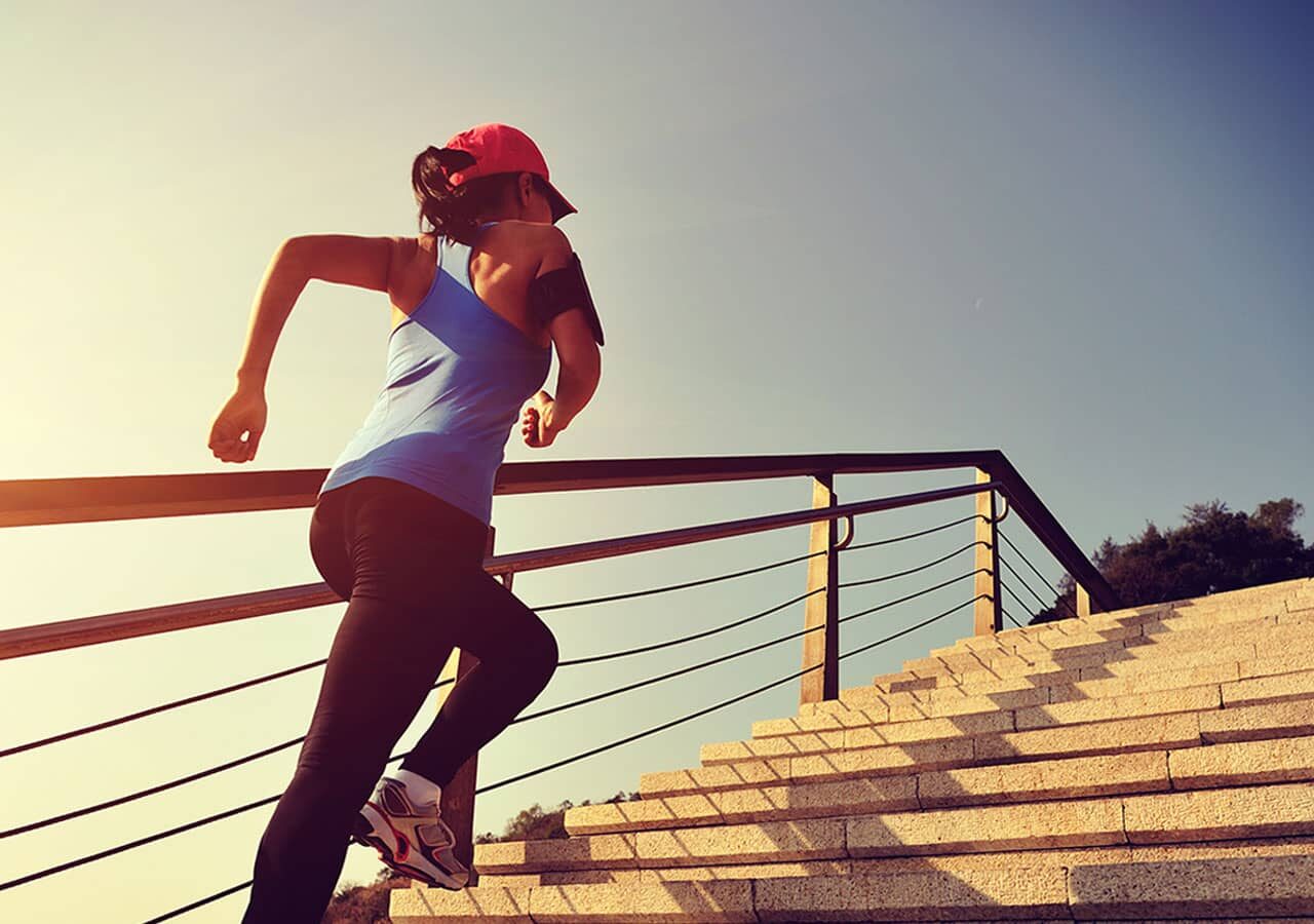 Vermögenswirksame Leistungen, Sportliche Frau joggt Treppe hoch, blauer Himmel im Hintergrund